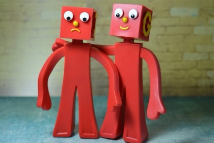 Illustration: Zwei rote Figuren, der eine legt den Arm um den anderen